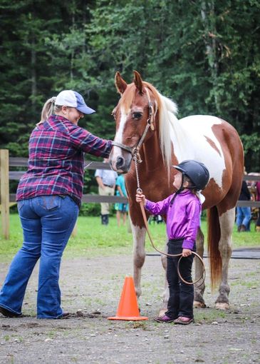 A woman and a young girl with a horse outdoors near a fence.