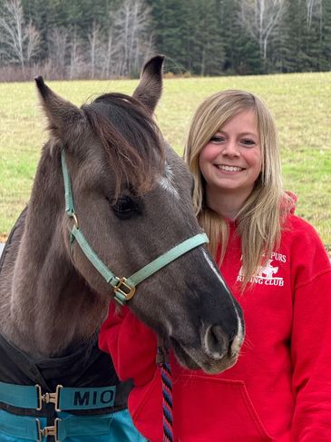 Smiling girl in red sweatshirt with a dark horse outdoors.