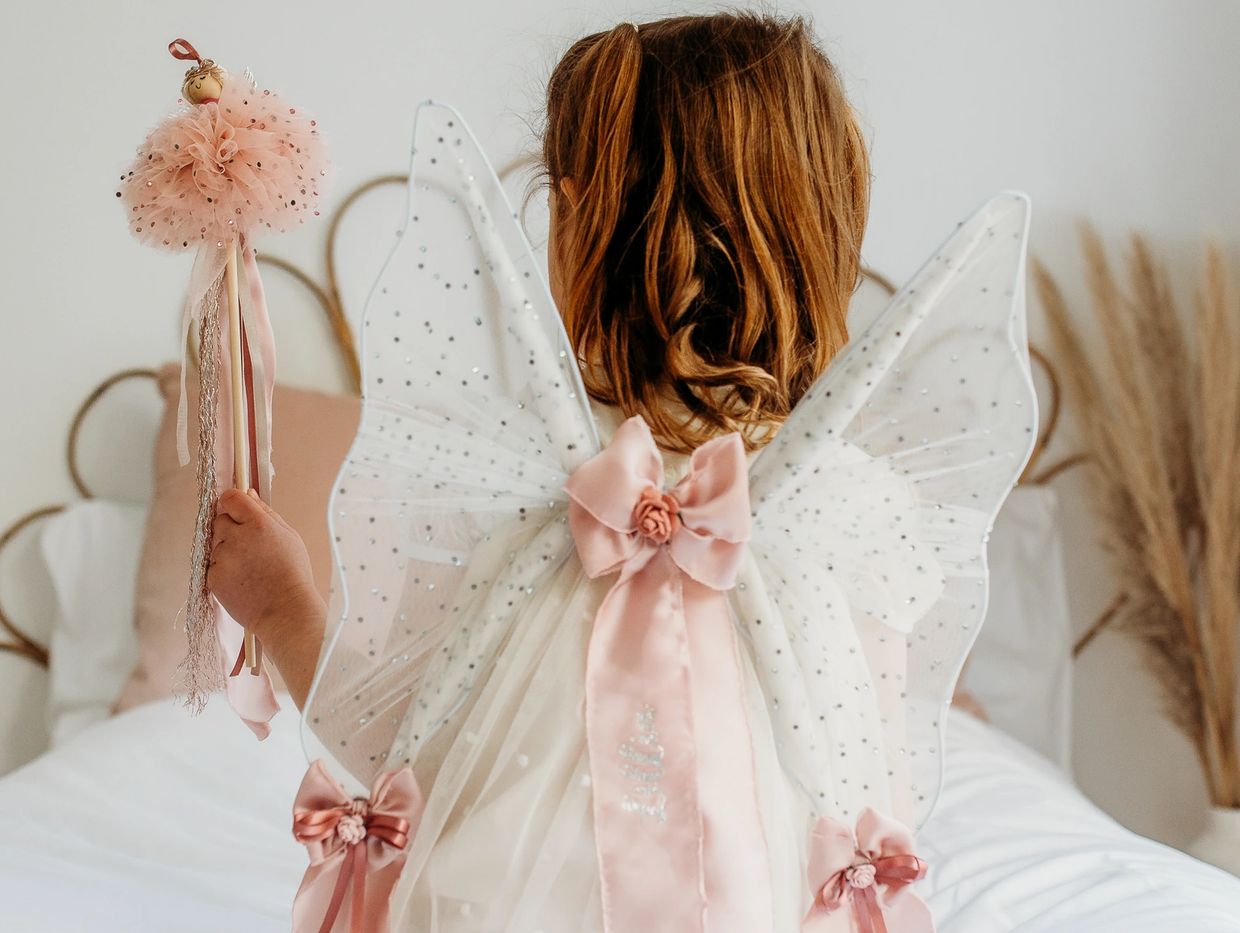 little girl with fairy wings and fairy wand sitting on bed in bedrrom