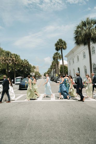 Wedding party crossing a sunny street lined with palm trees.