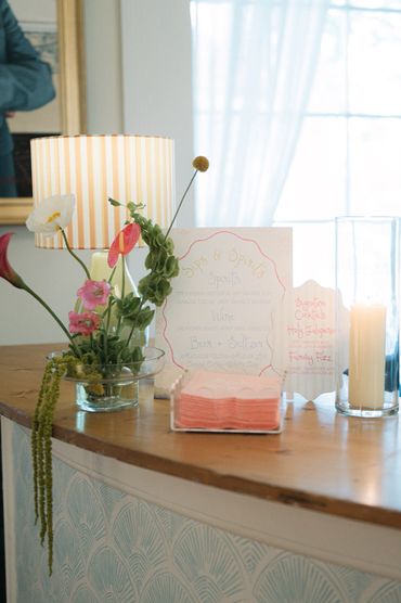 Decorative floral arrangement with lit candle and menu cards on a wooden surface.