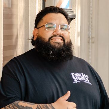 Bearded man wearing glasses and a barber-themed t-shirt giving a thumbs-up.