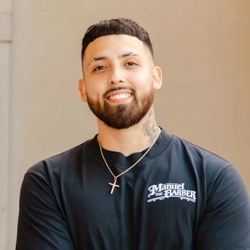 Smiling man with a beard wearing a Manuel the Barber shirt.