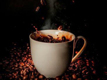 A steaming cup of coffee surrounded by coffee beans in low light.
