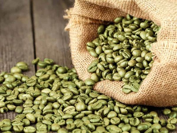 Green coffee beans spilling from a burlap sack onto a wooden surface.