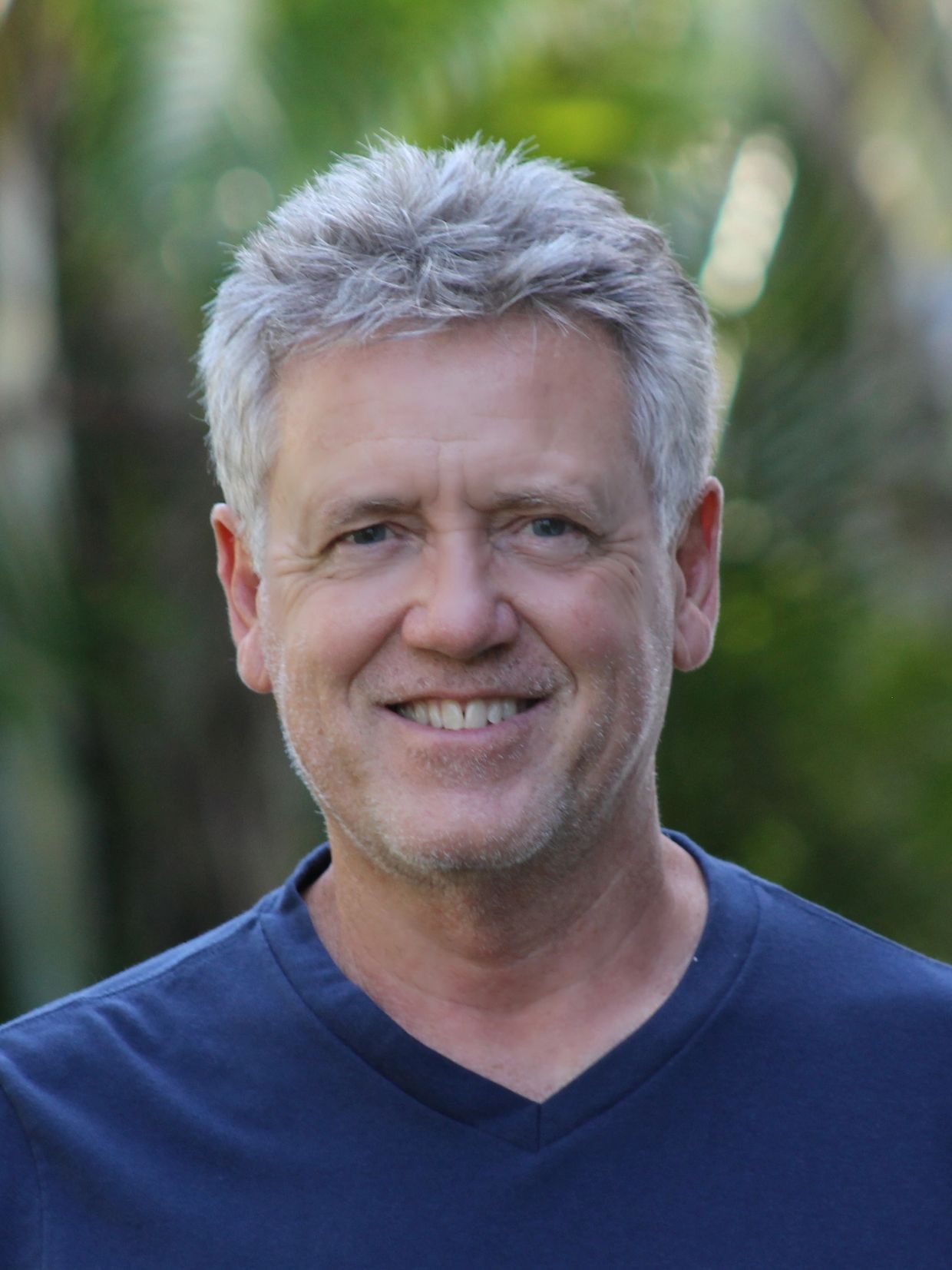 Smiling middle-aged man with gray hair wearing a blue shirt outdoors.