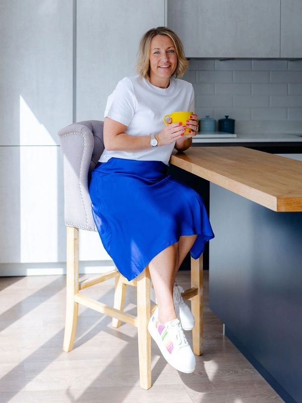 Woman sitting on a stool holding a yellow mug in a modern kitchen.