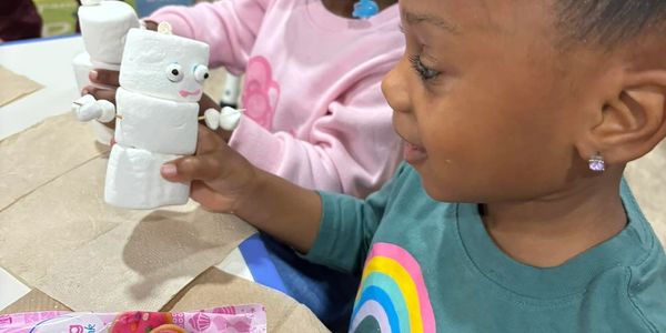 A child happily holding a marshmallow snowman craft at a table.