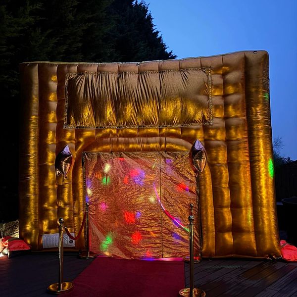Golden inflatable photo booth with colorful lights and red carpet at night.