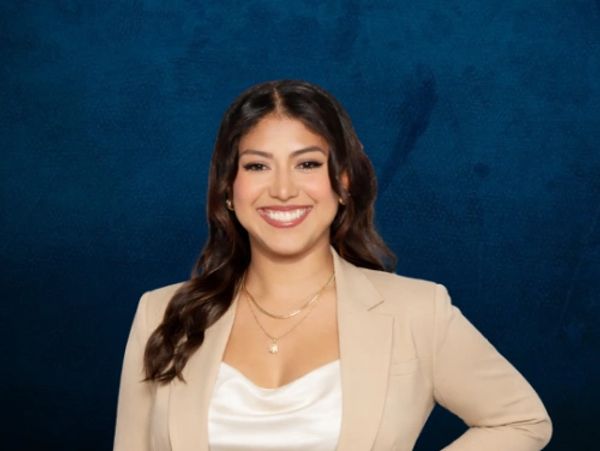 Smiling woman in a beige blazer against a dark blue background.