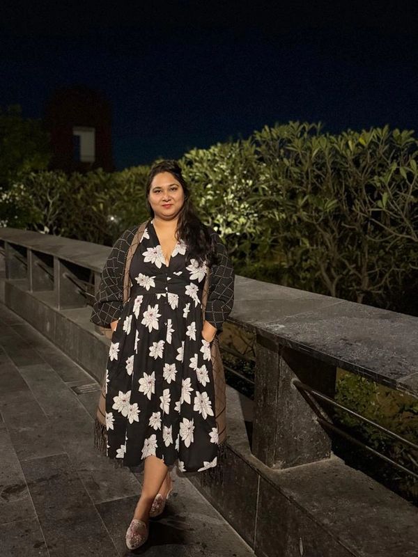 Woman in a floral dress posing outdoors at night near a stone railing.