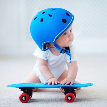 A baby with a blue helmet on, pushing a blue skateboard