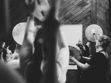 People playing hand drums in a group setting indoors.