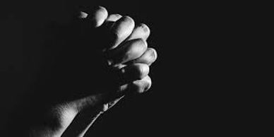 Two hands clasped tightly in a dark setting.