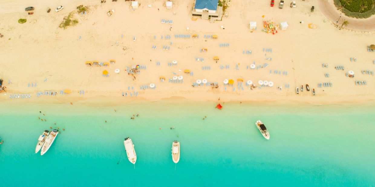 Vista aérea de playa con agua turquesa y botes anclados.