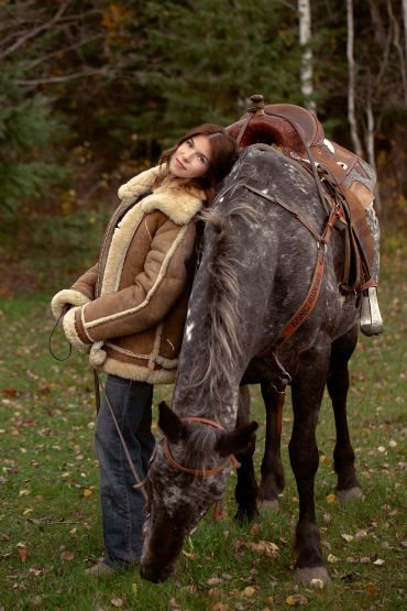Graduation Student in Cold Lake Alberta leaning against her horse in her ranch clothes.