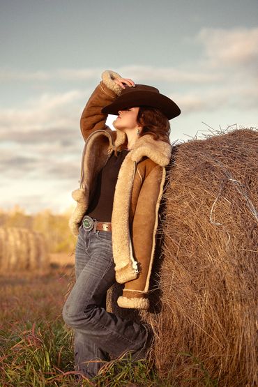 A Cold Lake Alberta Graduation student leaning against a hay bail in her Ranch attire.