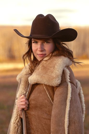 Graduation student in Cold Lake Alberta posing with her sheepskin coat and cowboy hat at sundown.