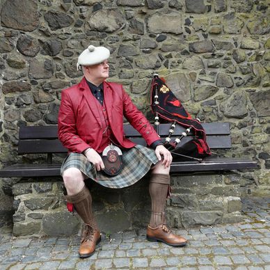 Man in traditional Scottish attire sitting on a bench with bagpipes.