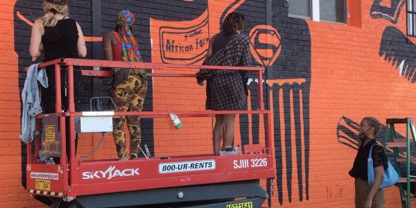 People painting a mural on an orange brick wall.