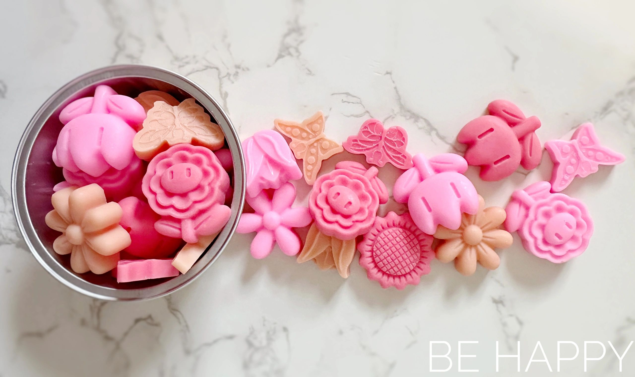 Colorful flower and butterfly-shaped soaps arranged on a marble surface.