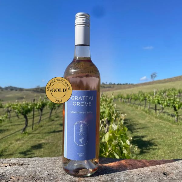 Bottle of Grattai Grove Sangiovese Rosé wine with a gold award, set against a vineyard backdrop.