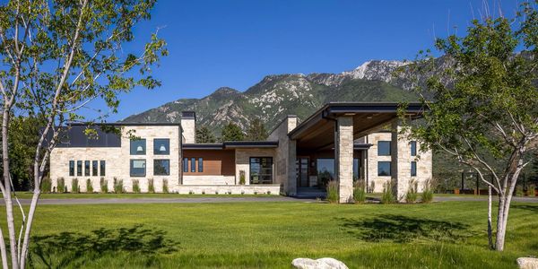 Modern house with mountain backdrop and green lawn.