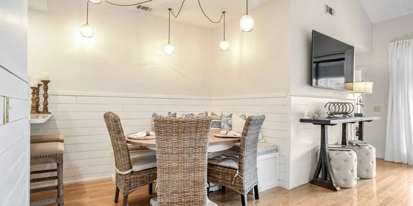 Coastal-style dining area with a round table, wicker chairs, built-in bench, and pendant lighting