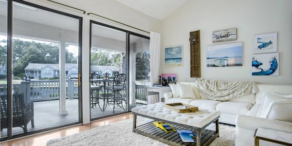 Sunlit living room with a white sectional, vaulted ceilings, and sliding doors leading to a deck