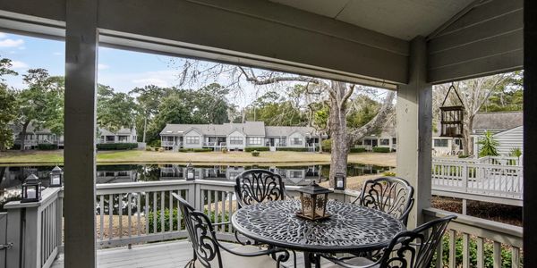 Outdoor deck with dining table, chairs, and a grill overlooking a peaceful lake in a Sea Pines rental.