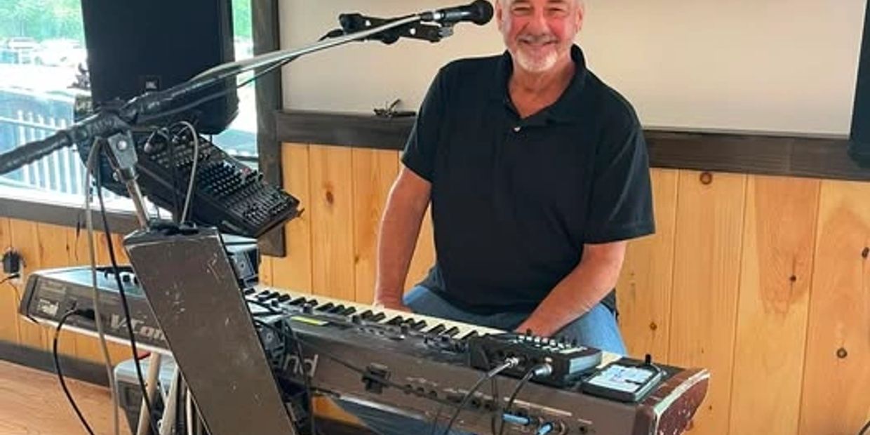 Smiling man sitting at keyboard with microphone.