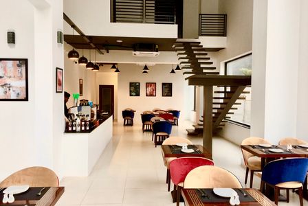 Restaurant interior. Open staircase. Seating with deep blue, red & light beige. Hanging art pieces.