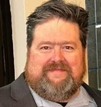 Bearded man in a suit smiling indoors.