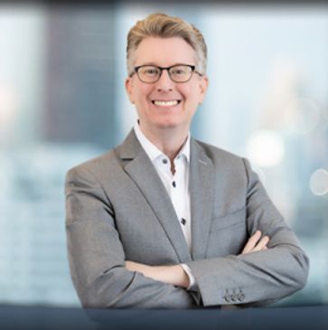 Smiling professional man in glasses and gray suit with arms crossed.