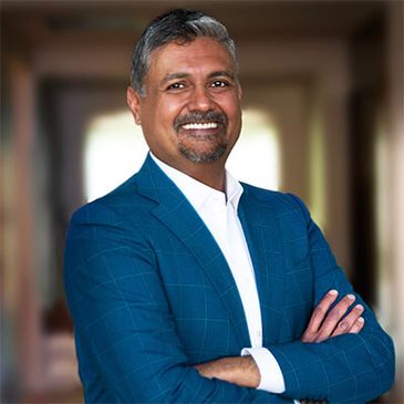 Confident man in blue suit smiling with arms crossed indoors.