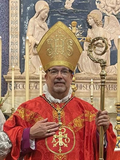 A bishop in ornate red and gold vestments holding a staff.