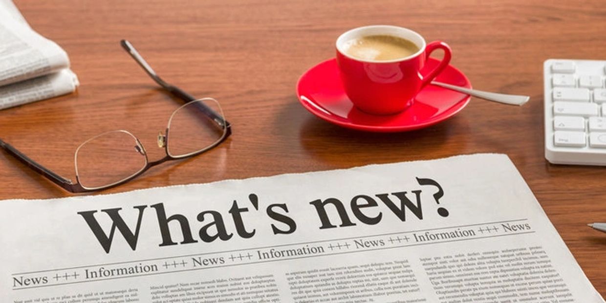 Newspaper titled "What's new?" on a desk with coffee, glasses, and keyboard.