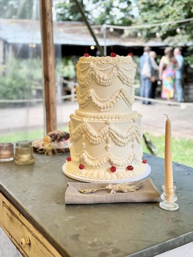 Two-tier white cake with elegant piped icing and cherries on top.