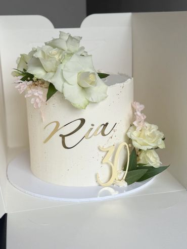 Elegant white cake decorated with fresh flowers and gold writing for a 30th birthday.