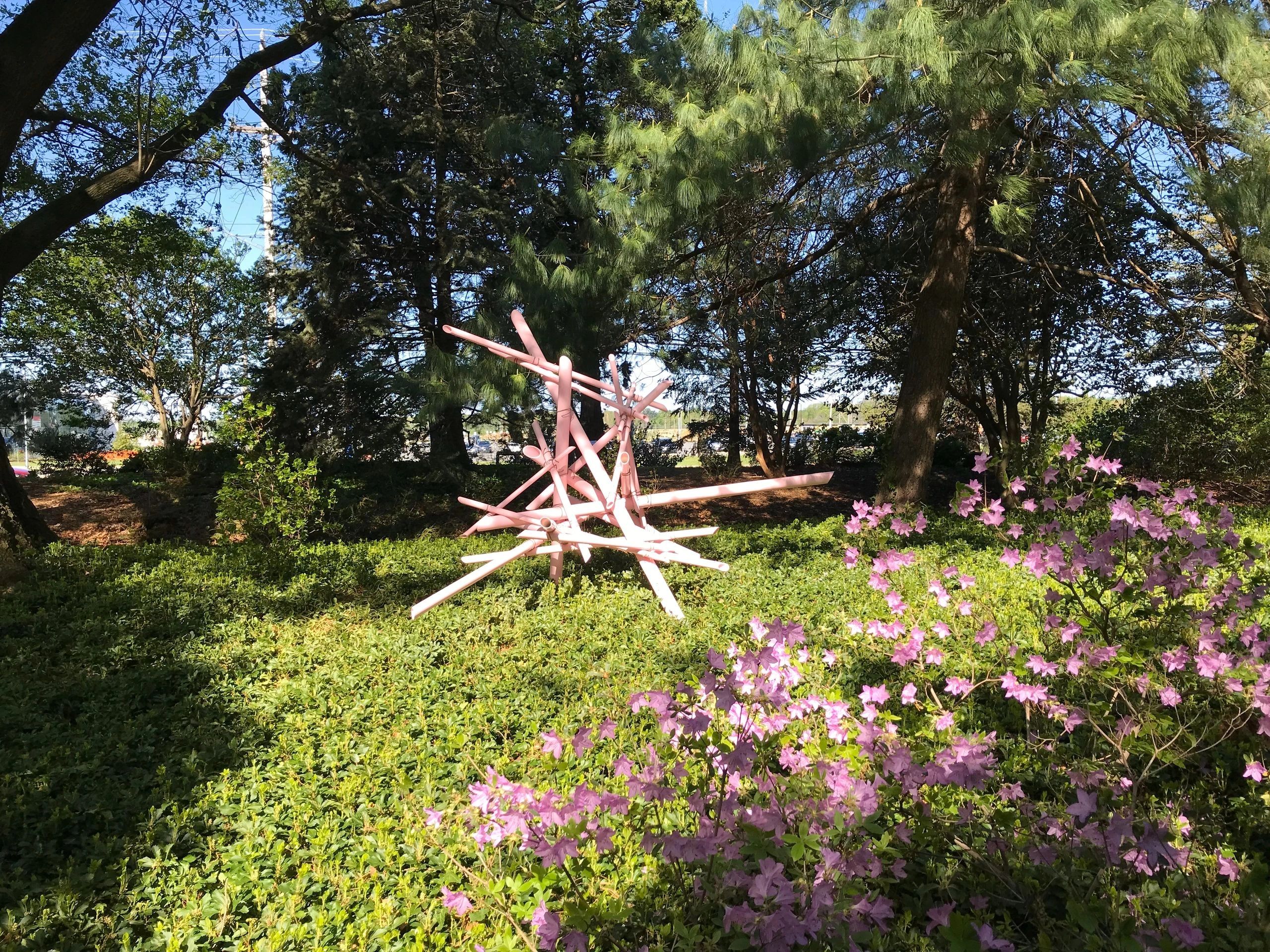 Pink metal sculpture in green garden with flowers.