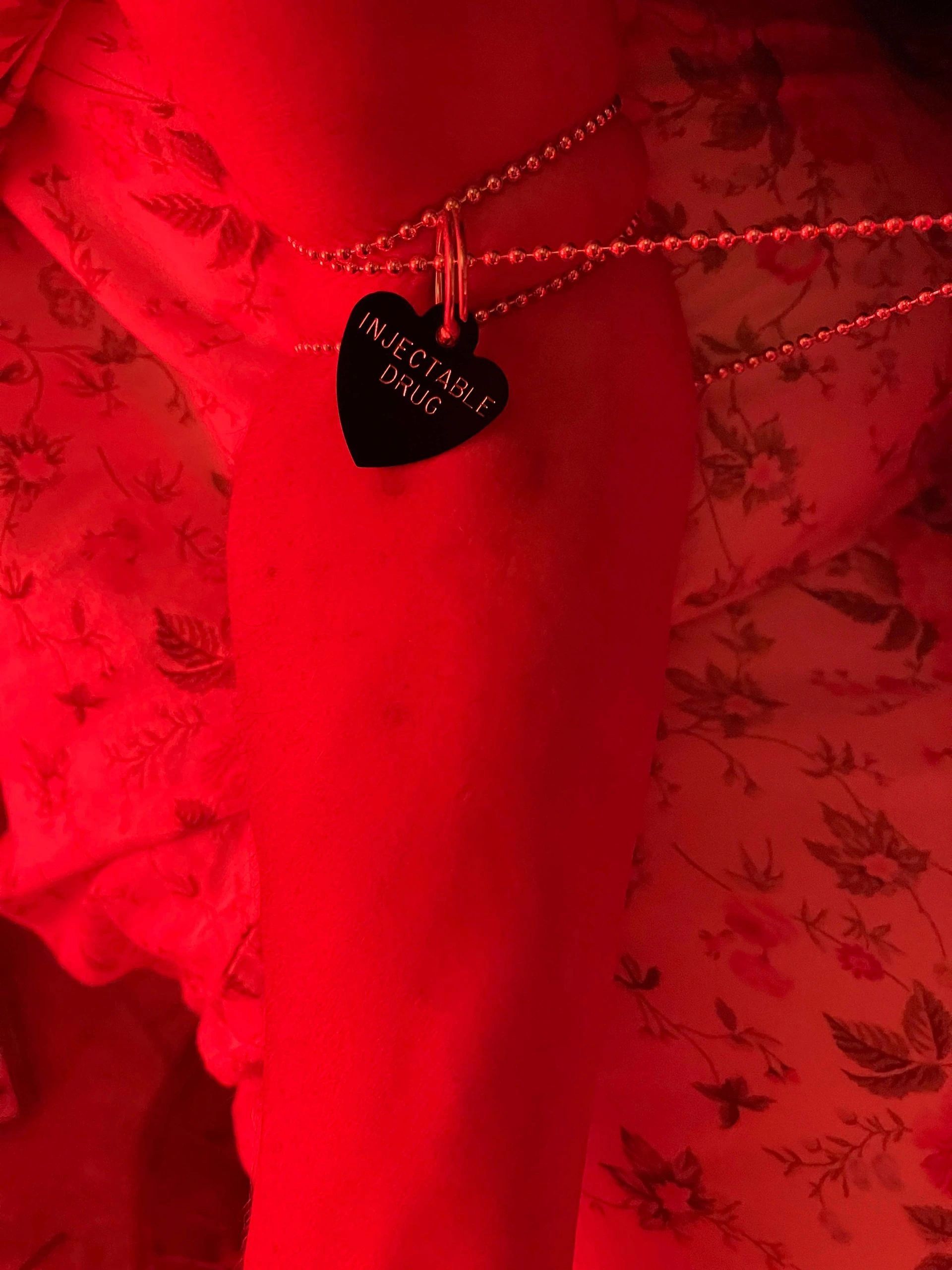 Heart-shaped tag with "INJECTABLE DRUG" on a red-lit arm with chains.