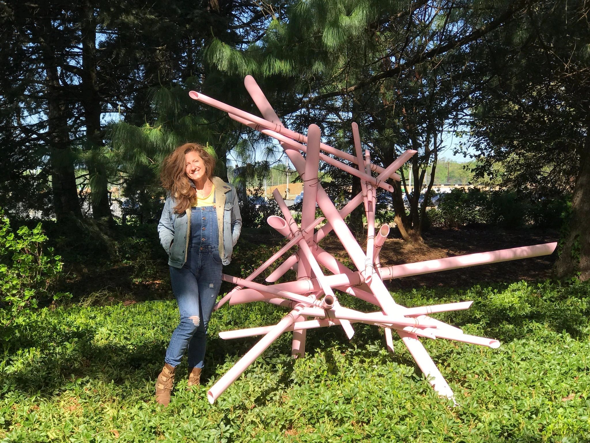 Woman standing next to pink abstract sculpture outdoors.