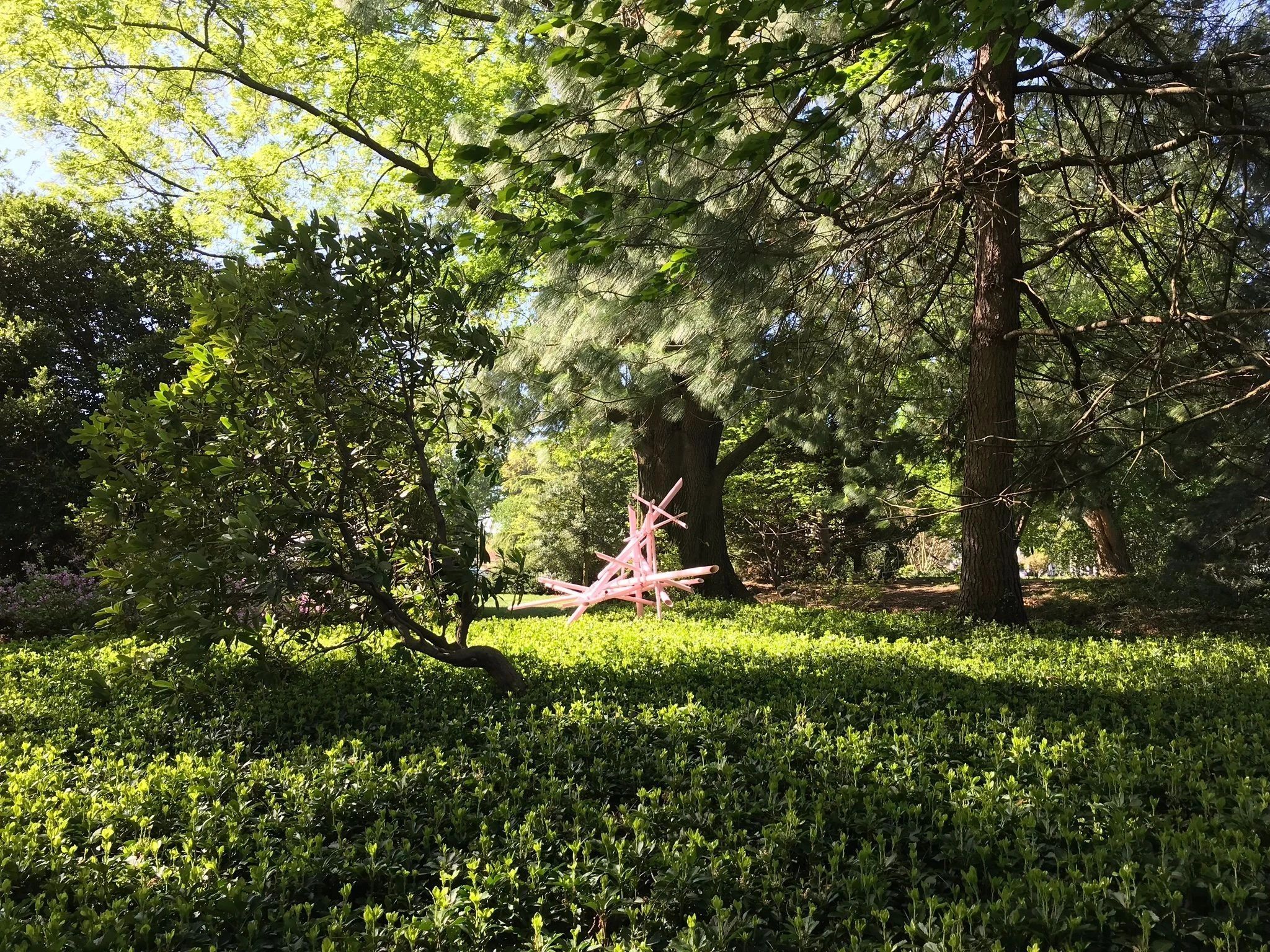 Green park with pink sculpture under tall trees.