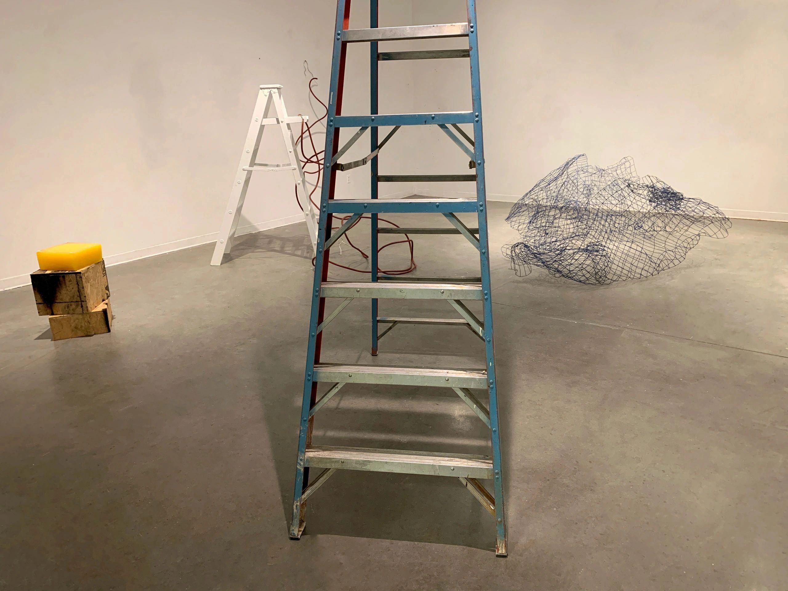 Two ladders and abstract art in an empty gallery space.