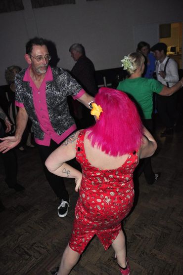 Two people dancing, one with bright pink hair and colorful outfits.