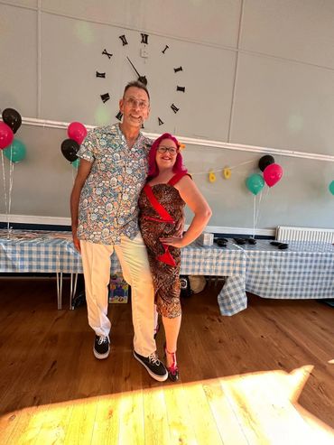 A happy couple poses in festive attire at a decorated party venue.