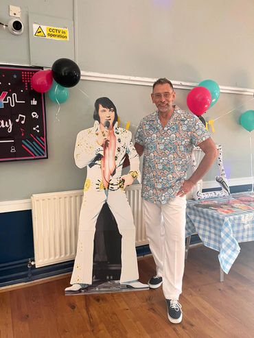 Man posing next to an Elvis Presley cardboard cutout at a decorated party.