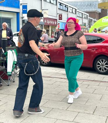 Couple dancing joyfully on a street with colorful attire.