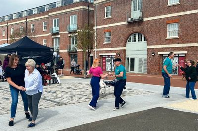 People dancing outdoors in pairs near a brick building.