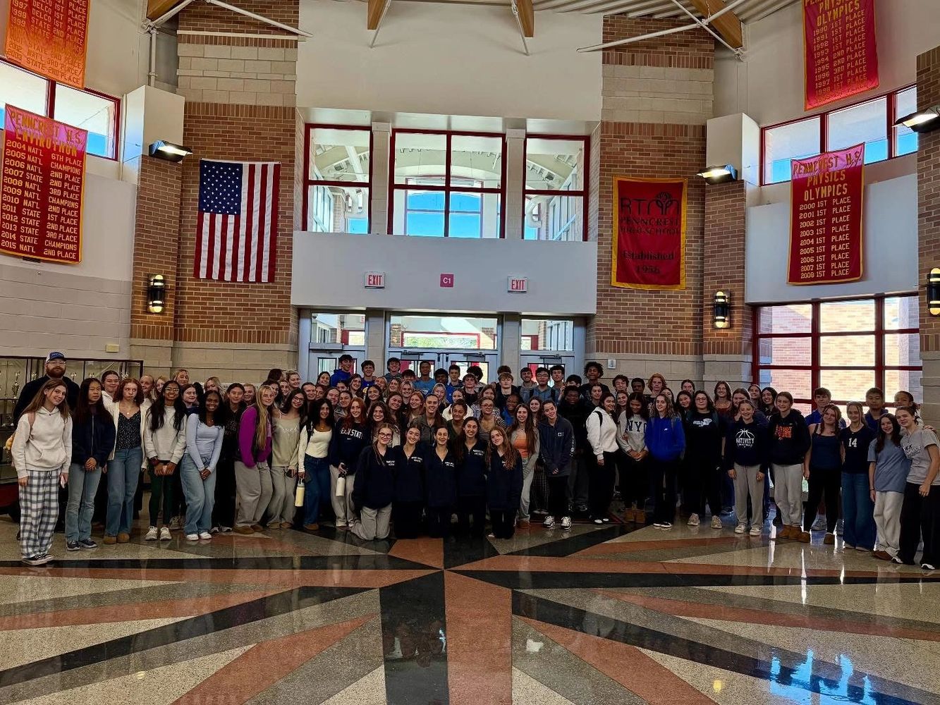 Large group of students gathered in a school lobby with banners and an American flag.